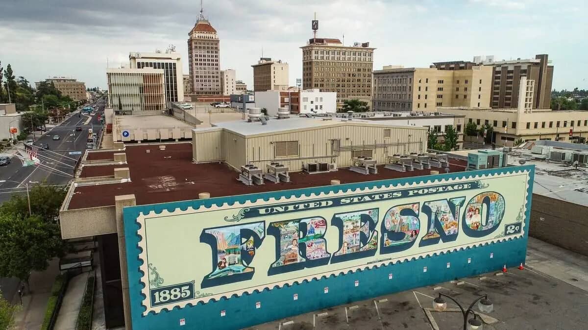 The Fresno postage stamp mural, dated 1885, on a downtown Fresno building with the city skyline behind it
